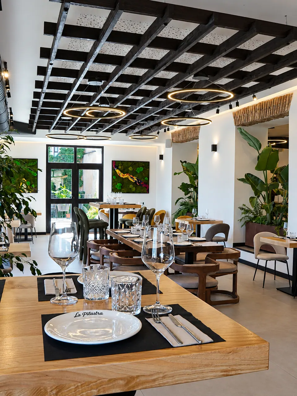 Interior de La Pilastra, con mesas de madera, vegetación y luz natural