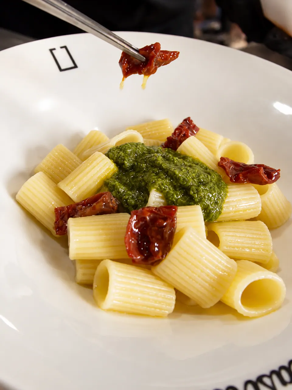 Rigatoni con pesto y tomate seco terminado con pinzas